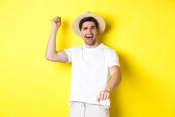 Concepto de turismo y verano. Joven viajero mostrando gesto de rodeo, de pie en sombrero de paja y ropa blanca, de pie sobre fondo amarillo — Foto de Stock