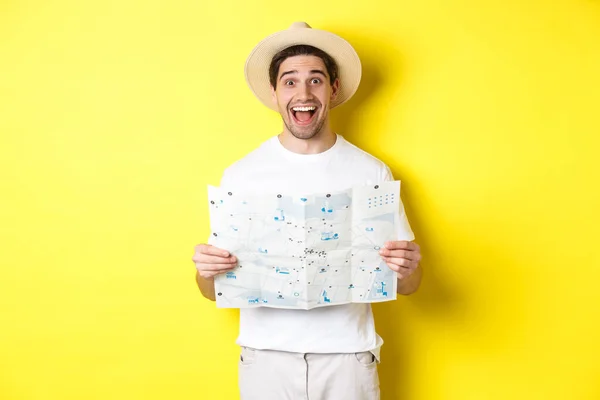Reiseliv, ferie og turisme. Spennende manneturist på sightseeing med kart, stående over gul bakgrunn – stockfoto