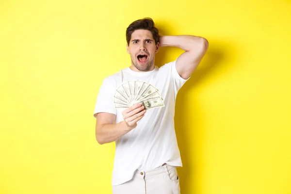 Hombre frustrado sosteniendo el dinero, gritando y entrando en pánico, de pie sobre el fondo amarillo — Foto de Stock