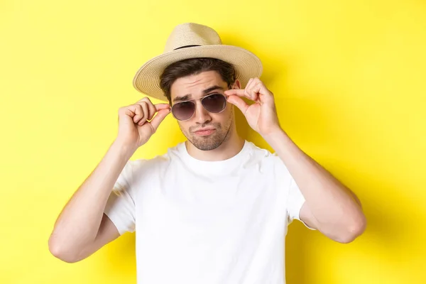 Concepto de turismo y vacaciones. Primer plano del turista fresco disfrutando de vacaciones de viaje, con gafas de sol con sombrero de paja, fondo amarillo — Foto de Stock