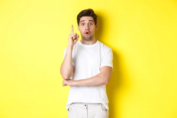 Tankeväckande kille föreslår lösning, höja fingret i Eureka tecken och ser upphetsad, har en idé, står mot gul bakgrund — Stockfoto