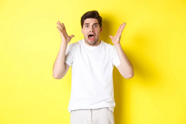 Frustrerad och chockad kille panik, skrikande och ser rädd, stående i vit t-shirt över gul bakgrund — Stockfoto