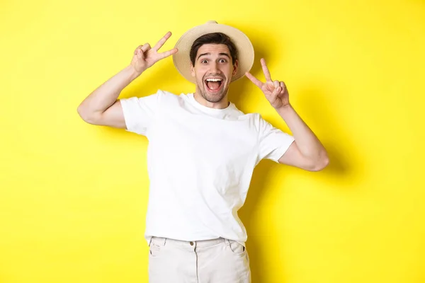 Концепция туризма и отдыха. Счастливый мужчина турист позирует для фото с знаками мира, улыбаясь взволнован, стоя на желтом фоне — стоковое фото