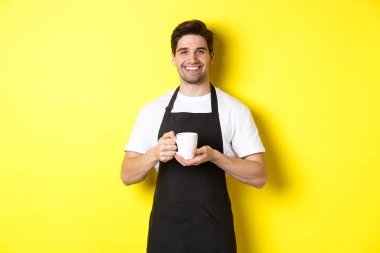 Kahve servisi yapan yakışıklı barista, fincanı getir, dostane bir gülümsemeyle siyah önlük içinde dur.