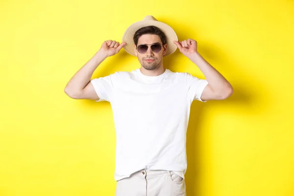 黄色の背景に立って、わらの帽子とサングラスを身に着けて、休暇の準備ができて若い男性観光客を自信を持って — ストック写真