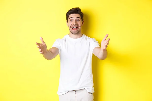 Emocionado cara bonito esticando as mãos para a frente, alcançando para abraço, recebendo presente, de pé sobre fundo amarelo — Fotografia de Stock