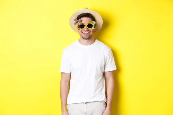 Concepto de turismo y vacaciones. Hombre sonriente relajado disfrutando de un viaje de cena, con gafas de sol y sombrero de paja, fondo amarillo — Foto de Stock