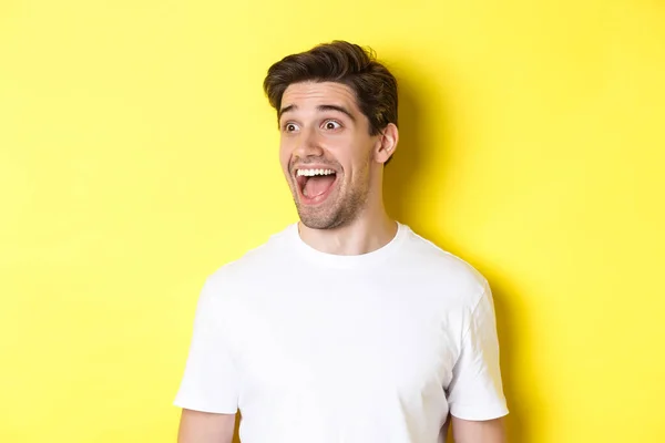 Imagen del hombre feliz mirando la promo, mirando a la izquierda con asombro, de pie en camiseta blanca sobre fondo amarillo — Foto de Stock