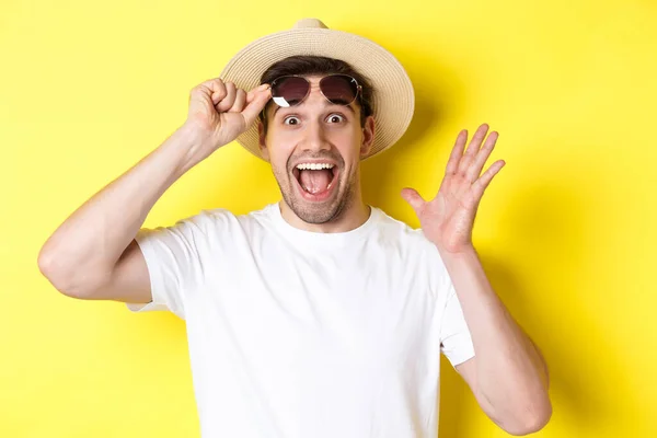 Concepto de turismo y vacaciones. Emocionado hombre turista tomar-off gafas de sol y mirando sorprendido en la oferta promocional, de pie sobre fondo amarillo — Foto de Stock