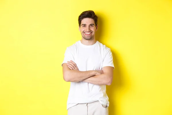 Bilde av en selvsikker kaukasisk mann som smilte fornøyd, holdt hender krysset på brystet og så fornøyd ut, stående over gul bakgrunn – stockfoto