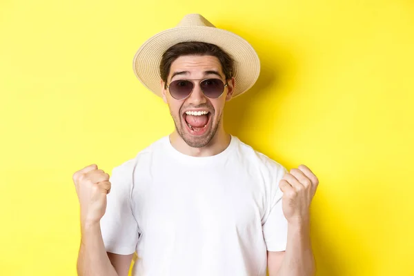 Concepto de turismo y vacaciones. Hombre afortunado turista ganando boletos, haciendo puño bomba y diciendo que sí, usando ropa de vacaciones, de pie sobre fondo amarillo — Foto de Stock