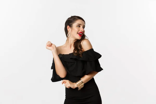 Moda e beleza. Mulher comemorando e dançando em vestido preto, se divertindo e sorrindo, de pé sobre fundo branco — Fotografia de Stock