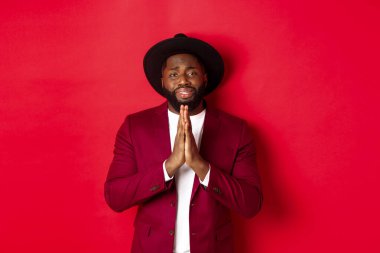 Sefil siyah adam yardım istiyor, yardım dileniyor ve üzgün görünüyor, kırmızı arka planda duruyor.