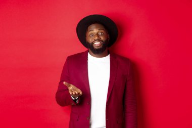 Yakışıklı gülümseyen siyah adam seni tebrik ediyor, kameraya gururla el kaldırıyor, övgüler yağdırıyor, kırmızı arka planda duruyor.