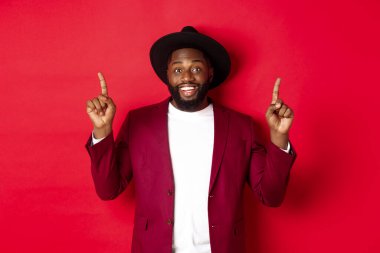 Kış tatili ve alışveriş konsepti. Parti kıyafetli neşeli Afro-Amerikalı adam logoyu gösteriyor ve gülümsüyor.