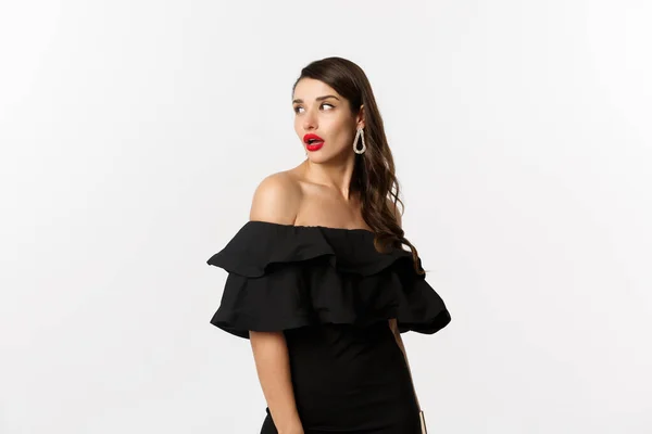 Fashion and beauty concept. Image of attractive young woman in black dress turn behind and looking at copy space, standing over white background — Stock Photo, Image