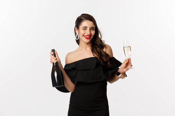 Celebration and party concept. Stylish brunette woman in glamour dress holding bottle and glass of champagne, having fun on new year holiday