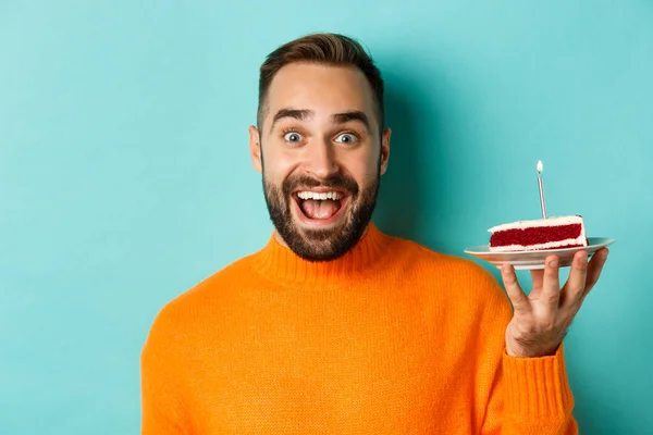Close-up van de gelukkige volwassen man vieren verjaardag, houden van bday cake met kaars en het maken van wens, staan tegen turquoise achtergrond — Stockfoto