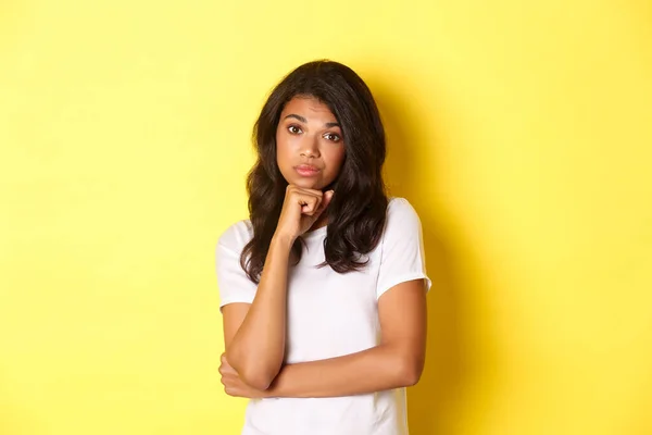 Portret van een ongeamuseerd en verveeld Afrikaans-Amerikaans tienermeisje dat met tegenzin naar de camera keek en over een gele achtergrond stond — Stockfoto