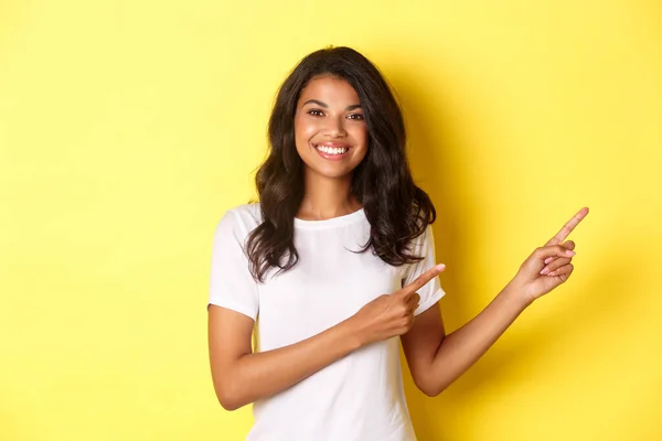 一个快乐的非洲裔美国少女的画像，面带微笑，手指指向信息横幅，展示复制的空间，站在黄色的背景上 — 图库照片