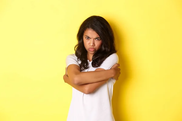 Bild eines launischen süßen afrikanisch-amerikanischen Mädchens, das sich umarmt und mit beleidigtem Gesichtsausdruck schmollt, auf gelbem Hintergrund stehend — Stockfoto