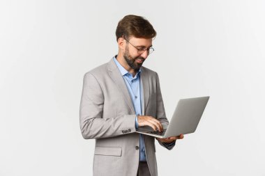 Yakışıklı, başarılı bir iş adamının gri takımlı ve dizüstü bilgisayarı beyaz arka planda dururken görüntüsü.