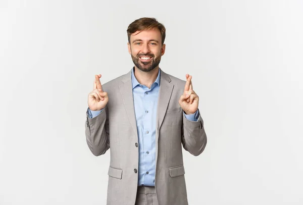 Retrato de bem sucedido sorridente empresário fazendo desejo, cruzando os dedos para a boa sorte, à espera de resultados, de pé sobre fundo branco — Fotografia de Stock