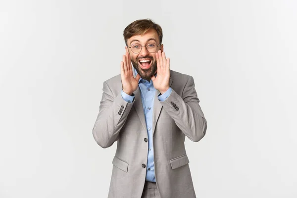 Retrato de homem de negócios feliz em terno cinza e óculos, fazendo anúncio, gritando alto e procurando por funcionários, de pé sobre fundo branco — Fotografia de Stock