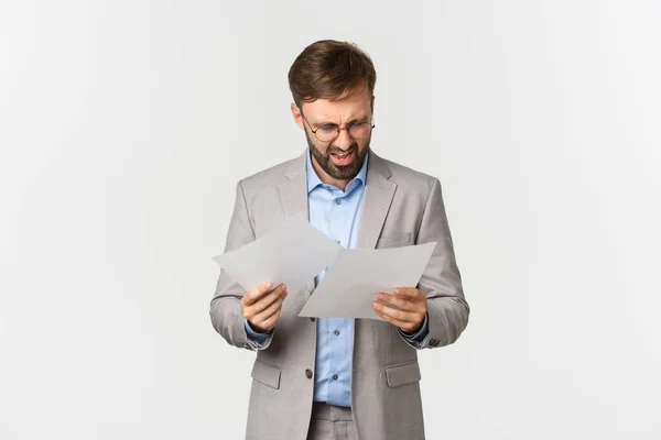 Retrato de hombre de negocios enojado y confundido en traje gris, mirando documentos o mal informe, de pie decepcionado por el fondo blanco — Foto de Stock