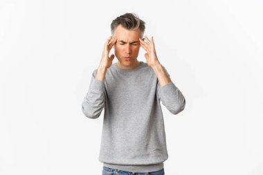 Gri kazaklı orta yaşlı bir adamın portresi baş ağrısı, baş ağrısı ve acı veren migrenden dolayı buruşma, beyaz arka planda duruyor.