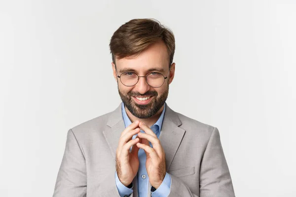 Close-up de empresário barbudo em óculos e terno, planejando algo, sorrindo tortuoso e tendo plano perfeito, em pé sobre fundo branco — Fotografia de Stock