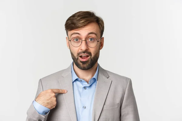 Primer plano del trabajador de oficina sorprendido y emocionado en gafas y traje gris, señalando con el dedo a la cámara y mirando confundido, de pie sobre fondo blanco — Foto de Stock