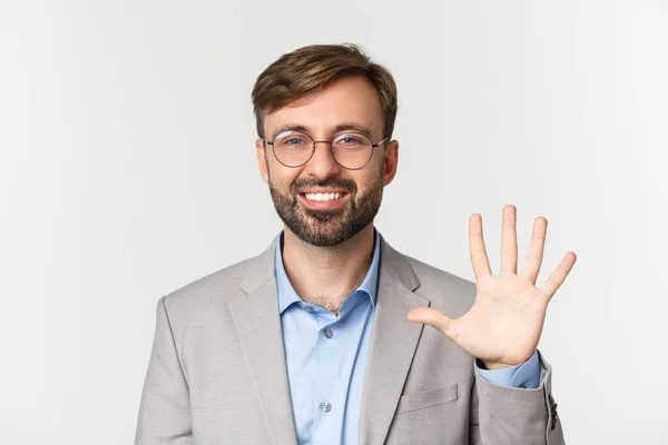 Close-up de homem barbudo bonito em óculos e terno cinza, mostrando o número cinco e sorrindo, de pé sobre fundo branco — Fotografia de Stock