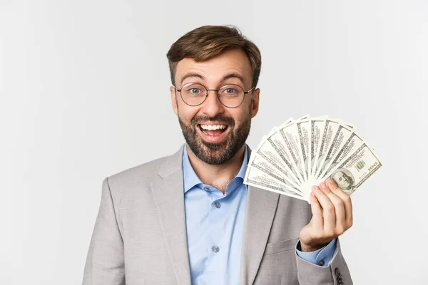 Primer plano del empresario masculino feliz en gafas y traje gris, recibiendo ingresos de los negocios, mostrando dinero, de pie sobre fondo blanco — Foto de Stock