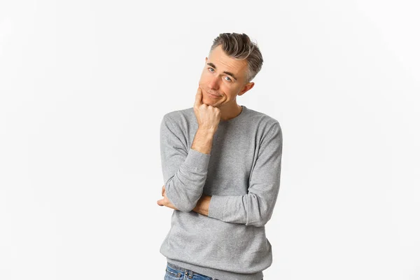 Portret van verveelde en ongeamuseerde man van middelbare leeftijd in grijze trui, leunend op de hand en kijkend naar camera terughoudend, droevig staande over witte achtergrond — Stockfoto