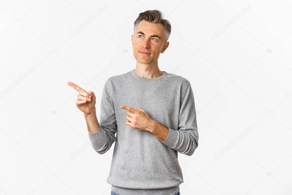 Image of thoughtful middle-aged man making choice, looking and pointing left, standing over white background.