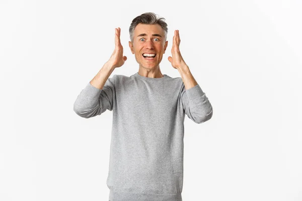 Image d'un homme d'âge moyen frustré en pull gris paniquant, serrant la main et regardant en détresse, debout sur fond blanc — Photo