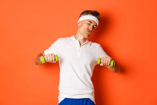 Képek a boldog középkorú srác csinál sport, edzés súlyzókkal, álló felett narancs háttér — Stock Fotó