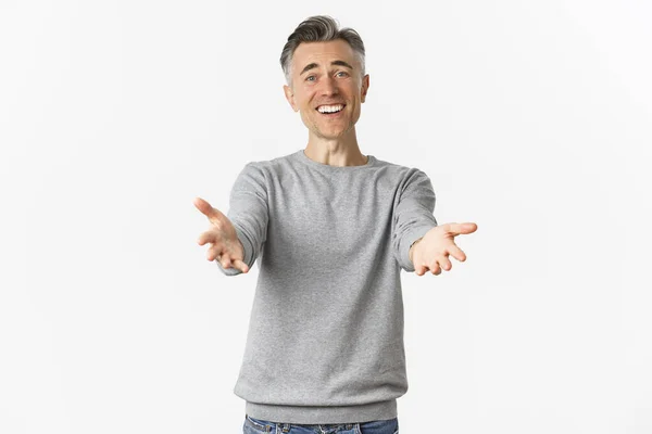 Imagem de homem de meia-idade feliz e satisfeito com cabelos grisalhos, estendendo as mãos para frente para abraçar ou acolher alguém, sorrindo aliviado, em pé sobre fundo branco — Fotografia de Stock