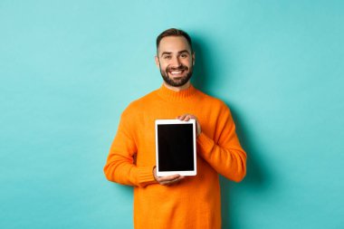 Teknoloji. Gülümseyen yakışıklı adam dijital tablet ekranı gösteriyor, uygulamayı gösteriyor, turkuaz arka planda duruyor