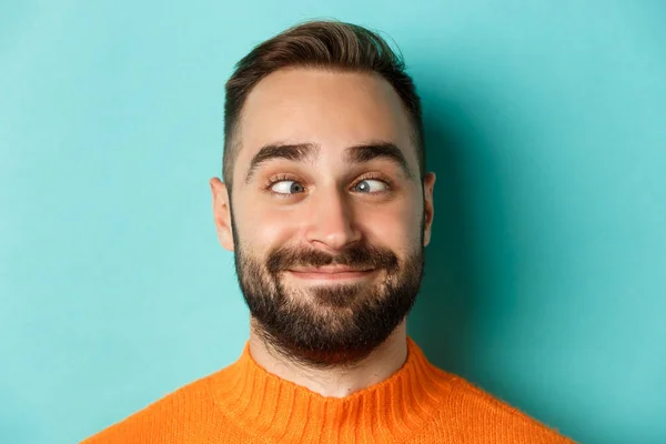 Headshot de hombre caucásico divertido haciendo caras, entrecerrando los ojos y sonriendo tonto, de pie sobre fondo azul claro — Foto de Stock