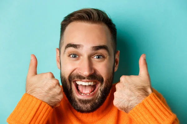 Headshot of excited bearded man showing thumbs-up, praising something good, approve and like product, standing over turquoise background — Stock Photo, Image