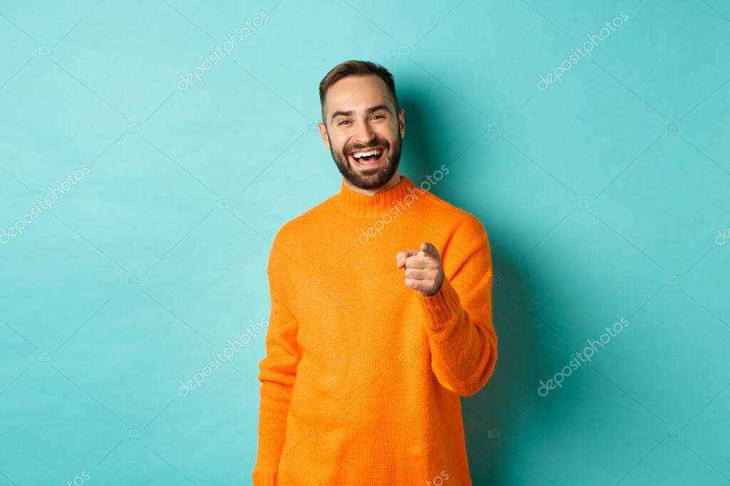 Handsome man laughing and pointing at camera, nodding in approval, agree with you, standing over light blue background.