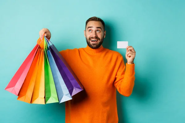 Feliz hombre aduly mostrando tarjetas de crédito y bolsas de compras, de pie sobre fondo turquesa — Foto de Stock