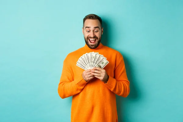 Imagen del hombre mirando feliz al dinero, sonriendo asombrado, de pie sobre fondo azul claro — Foto de Stock