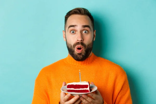 Close-up de homem adulto feliz comemorando aniversário, segurando bolo bday com vela e fazendo desejo, de pé contra fundo turquesa — Fotografia de Stock