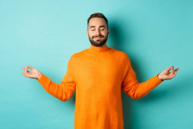 Rahatlamış ve rahatlamış bir adamın görüntüsü. Gözleri kapalı ve gülümseyen, stresten arınmış, sakin bir ifadeyle meditasyon yapan, açık mavi arka planda duran.