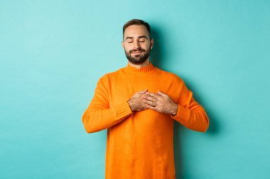 Yakışıklı adam nostaljik hissediyor, kalbi tutuyor ve hayal kuruyor, bir şeyleri hatırlıyor ya da hayal ediyor, turkuaz arka plana karşı kaygısız duruyor.