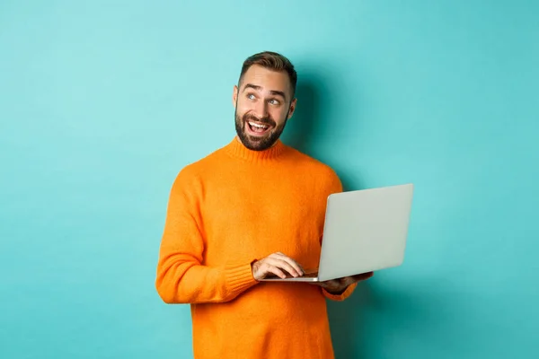 英俊的男人在网上购物，一边用笔记本电脑一边沉思，一边站在浅蓝色的背景上 — 图库照片