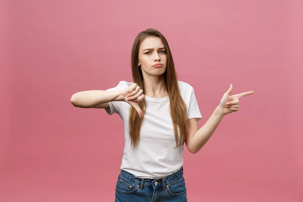 Primer plano de la mujer joven estricta seria lleva camisa blanca se ve estresado y apuntando hacia arriba con el dedo aislado sobre el fondo rosa — Foto de Stock
